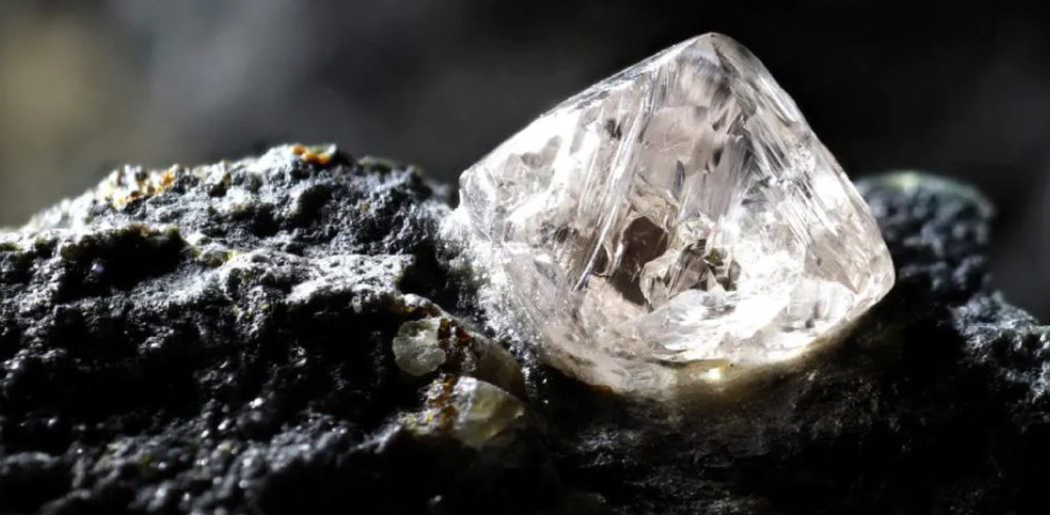 Natural diamond - A photo of a rough, uncut diamond found in nature. The photo shows a close-up of the diamond, which appears crystalline and has a multi-faceted surface with various angles and edges. Natural diamonds are formed deep within the Earth's mantle over millions of years under high pressure and temperature conditions. 