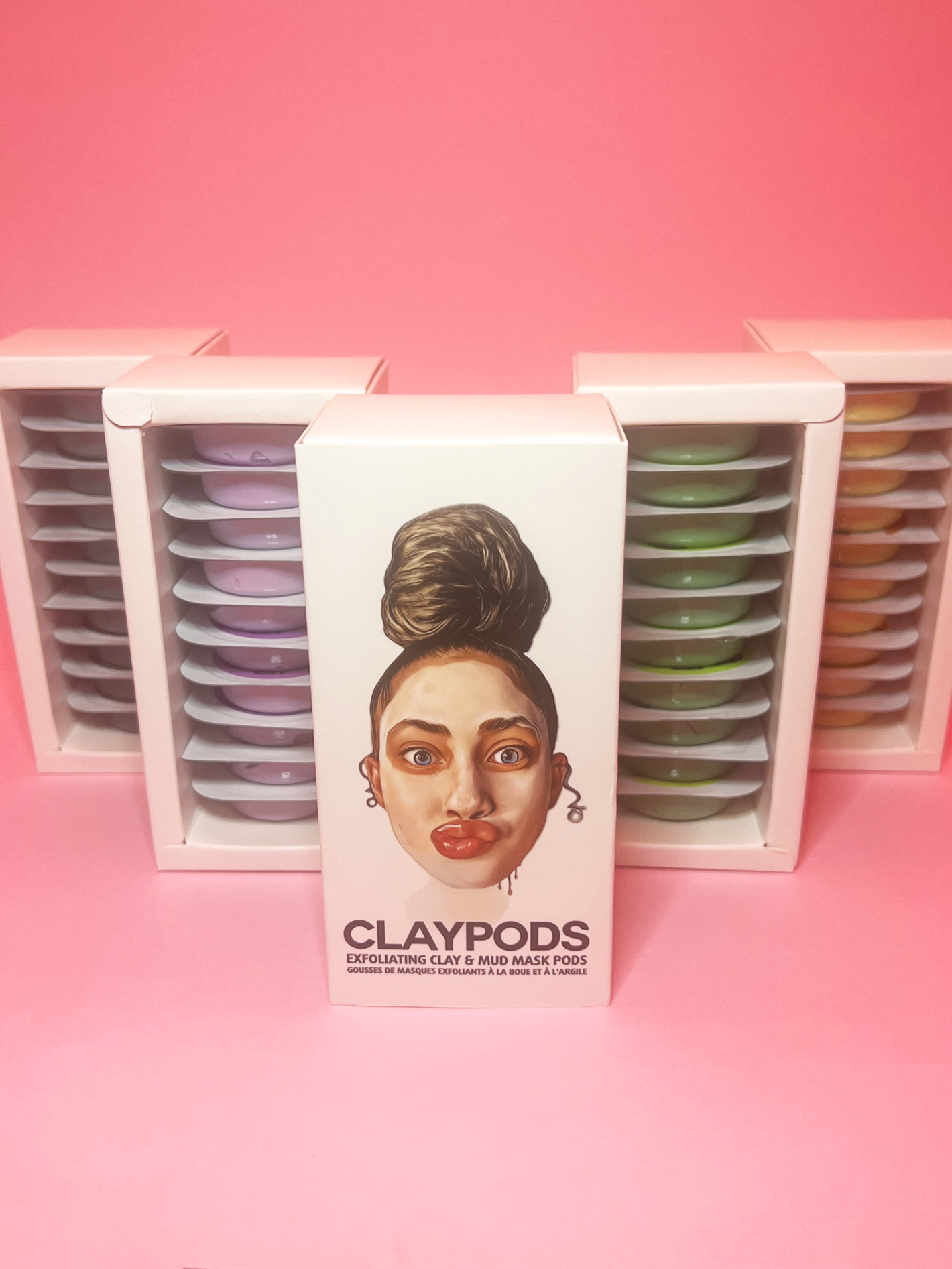 Clay pod blends, Avocado, Eggplant, Dead Sea, Turmeric on a pink background. Main box of clay ponds in front