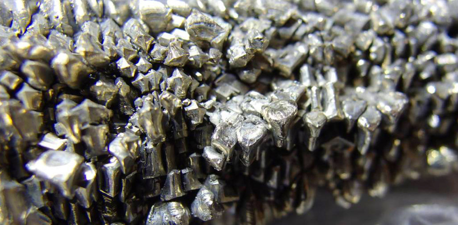 Titanium - A photo of a shiny metallic element, titanium, in the form of a rectangular bar. The surface of the titanium is reflective and appears silver or gray in color. It has a smooth texture and a high sheen, suggesting its metallic and lustrous properties. 